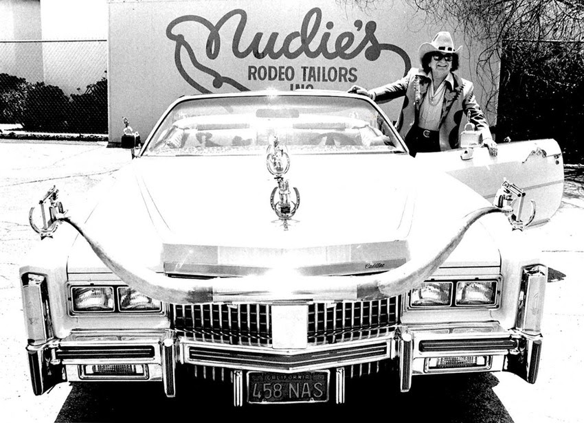 Cohn was equally famous for his garishly decorated automobiles. Between 1950 and 1975 he customized 18 vehicles, mostly white Pontiac Bonneville convertibles, with silver-dollar-studded dashboards, pistol door handles and gearshifts, extended rear bumpers, and enormous longhorn steer horn hood ornaments. Pictured here: Nudie with one his classic decorated Nudie Mobiles 